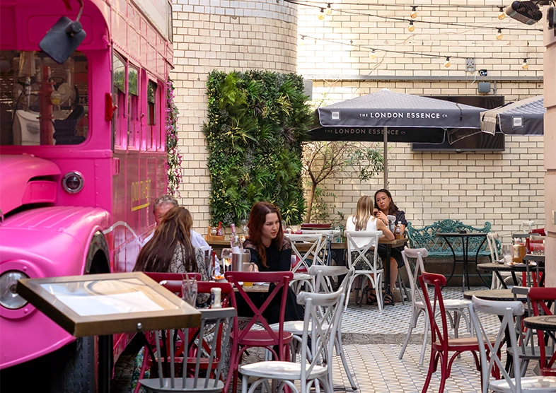 The Old Bank of England pub on Fleet Street in
London, features a vibrant pink vintage
Routemaster bus in its courtyard. The building,
once a branch of the Bank of England, has been
converted into a pub that serves traditional
British food and drinks. People are sat enjoying
drinks in the courtyard on a sunny day. 